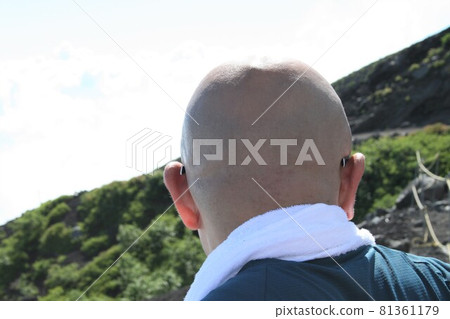Back view of a shaved-headed man climbing a mountain 81361179