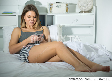 Smiling girl lying and using smartphone on bed in bedroom 81362512