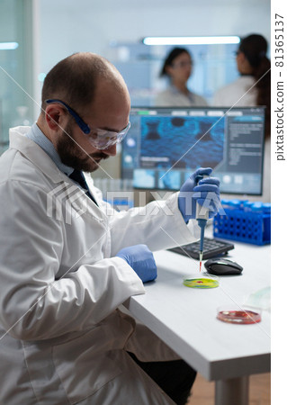 Scientist biologist man putting chemical fluid in petri dish using medical micropippete 81365137