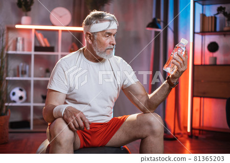 Senior man sitting on fitball with bottle of water in hand 81365203
