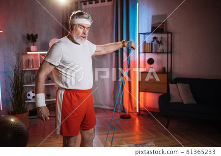 Muscular senior man training arms with resistance band 81365233