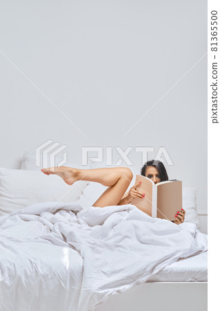 Young woman in bed stretching her leg out Young woman in bed stretching her leg out 81365500
