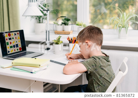 Distance learning online education. Caucasian smile kid boy studying at home with laptop and doing school homework. Thinking child siting with notebook, pencils and training books. Back to school 81365872