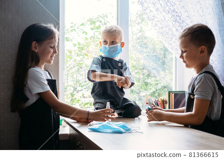 Back To School Safety. Schoolkids wearing masks and using antiseptic in classroom at school. hildren with face mask at school after covid-19 quarantine and lockdown 81366615