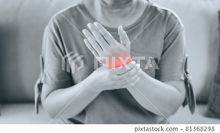 Closeup of woman sitting on sofa holds her wrist, hand injury with red highlight, feeling pain. Health care and medical concept. 81368298