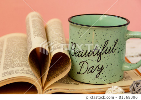 A green cup of tea stands on a book. Pink background. Eucalyptus flowers. The pages of the book are wrapped in the shape of a heart A green cup of tea stands on a book. Pink background. Eucalyptus flowers. The pages of the book are wrapped in the shape of a heart 81369396