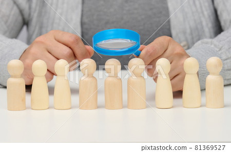 figurines of men on a white table, a female hand holds a magnifying glass over one. concept of searching for employees in the company 81369527