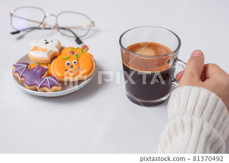 woman hand holding coffee cup during eating funny Halloween Cookies. Happy Halloween day, Trick or Threat, Hello October, fall autumn, Traditional, party and holiday concept 81370492