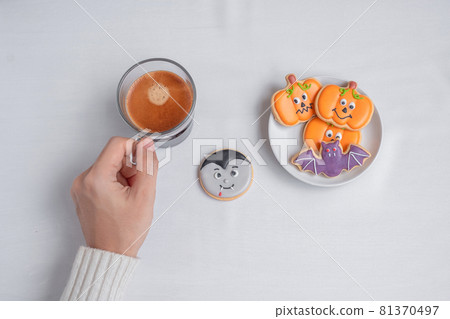 woman hand holding coffee cup during eating funny Halloween Cookies. Happy Halloween day, Trick or Threat, Hello October, fall autumn, Traditional, party and holiday concept 81370497