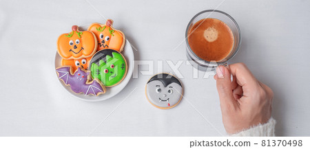 woman hand holding coffee cup during eating funny Halloween Cookies. Happy Halloween day, Trick or Threat, Hello October, fall autumn, Traditional, party and holiday concept 81370498