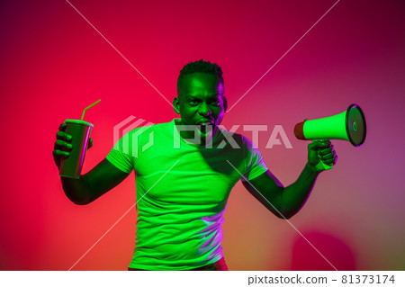 Creative image of African young man in casual clothes isolated on red color studio background in neon light, filter. Concept of human emotions, facial expression, youth, feelings, ad. Creative image of African young man in casual clothes isolated on red color studio background in neon light, filter. Concept of human emotions, facial expression, youth, feelings, ad. 81373174