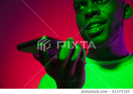Creative image of African young man in casual clothes isolated on red color studio background in neon light, filter. Concept of human emotions, facial expression, youth, feelings, ad. 81373185