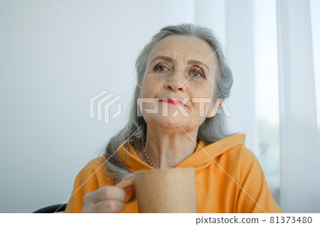 Elderly gray-haired woman is drinking coffee while sitting at home. Happy retirement 81373480