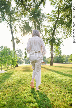 Back view of woman walking barefoot on lawn 81373548