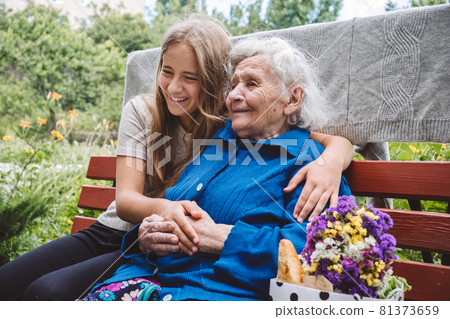 Grandparents Day, Reunited family, togetherness. Senior old grandma hugs granddaughter outdoors. Grandchild makes surprise for granny and gave her flowers 81373659