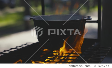 Cooking pot stands on a grate with a large flame of fire, cooking outdoors in a saucepan, outdoor tourist recipes, fiery dish on weekends, relaxing in the woods 81373733