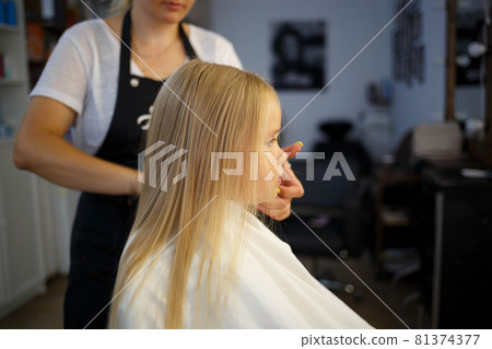 hairdresser straightens hair of a little girl in a beauty salon 81374377