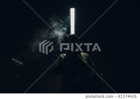 Portrait of young caucasian man smoking e-cigarette in dark with line light 81374426
