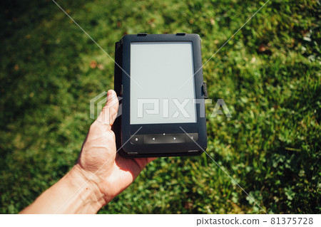 e-Book reader in hand, green grass background e-Book reader in hand, green grass background 81375728