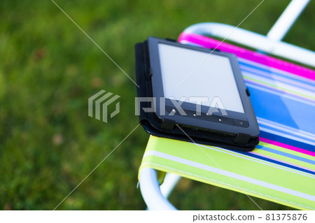 e-Book reader on the chair, green grass background e-Book reader on the chair, green grass background 81375876