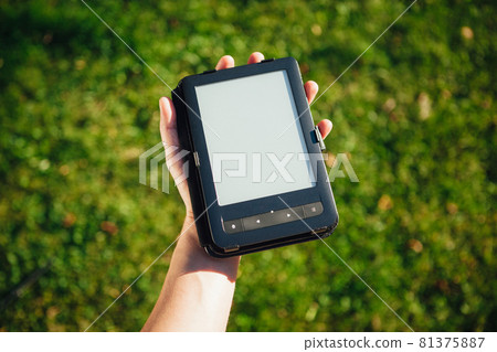 e-Book reader in hand, green grass background e-Book reader in hand, green grass background 81375887