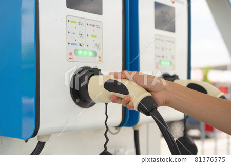 A hand holding cables from EV car charger or electric vehicle station. Cable connected at gas station, power supply battery charging an alternative eco environment future technology energy innovation A hand holding cables from EV car charger or electric vehicle station. Cable connected at gas station, power supply battery charging an alternative eco environment future technology energy innovation 81376575