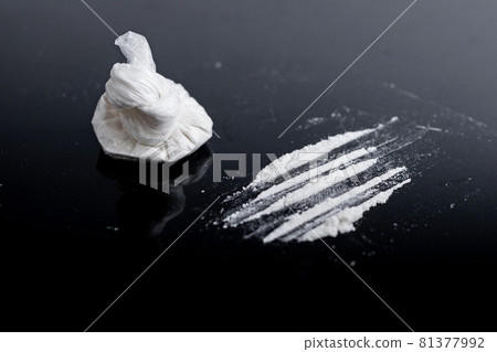 white powder (heroin, cocaine, narcotic) in a plastic bag on a black background, drugs are scattered in the form of a track 81377992