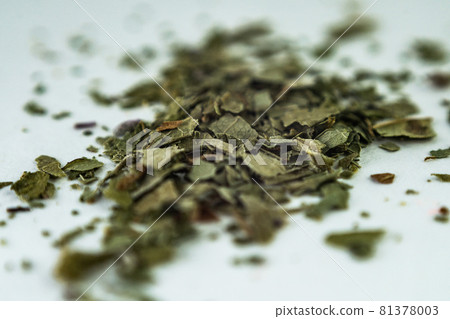 green dry crushed leaves (marijuana, tobacco) on a white surface green dry crushed leaves (marijuana, tobacco) on a white surface 81378003