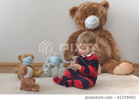 Child playing with his sick teddy bears wearing medical mask against viruses. Role playing, child playing doctor with plush toy. Children and illness concept. Child playing with his sick teddy bears wearing medical mask against viruses. Role playing, child playing doctor with plush toy. Children and illness concept. 81378403