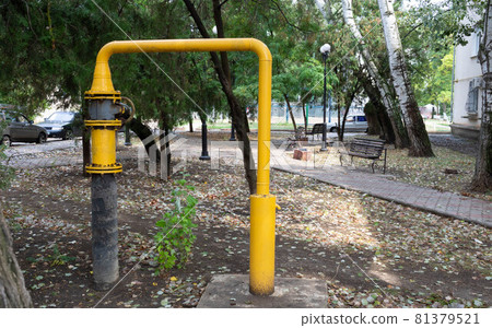 A yellow gas pipe with a valve stands in a public park A yellow gas pipe with a valve stands in a public park 81379521