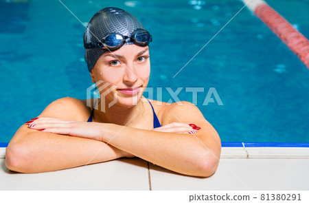 Portrait of Young smiling woman swimmer wearing goggles in indoor swimming pool 81380291