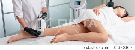 cosmetologist in rubber gloves doing endospheres therapy on female legs 81380300