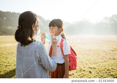 mother help her daughter to put on the mask before going to school mother help her daughter to put on the mask before going to school 81383600