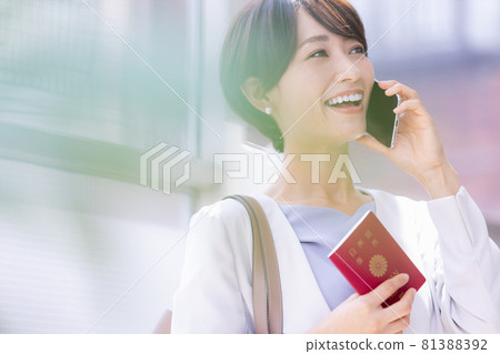 A woman holding a passport and talking on a smartphone A woman holding a passport and talking on a smartphone 81388392