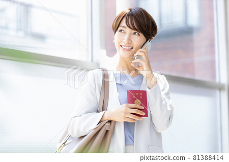 A woman holding a passport and talking on a smartphone A woman holding a passport and talking on a smartphone 81388414