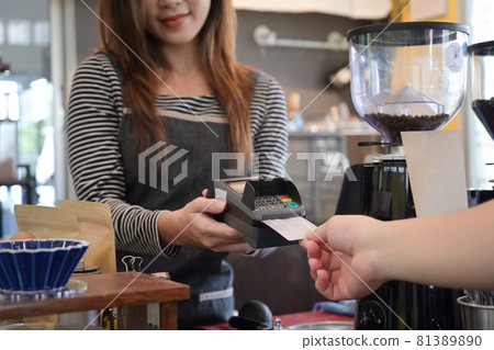 Female waiter holding credit card swipe machine while customer making payment in coffee shop with credit card. 81389890