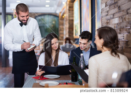 Waiter with notebook taking order from friendly company indoors Waiter with notebook taking order from friendly company indoors 81389924