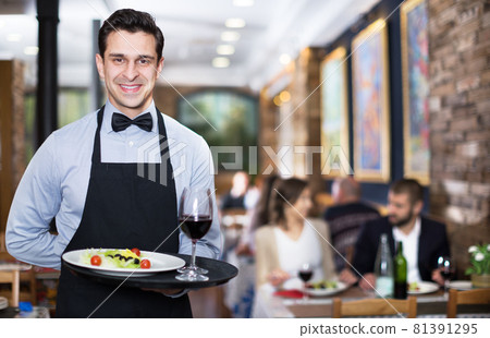 Smiling waiter with serving tray in restaurant Smiling waiter with serving tray in restaurant 81391295
