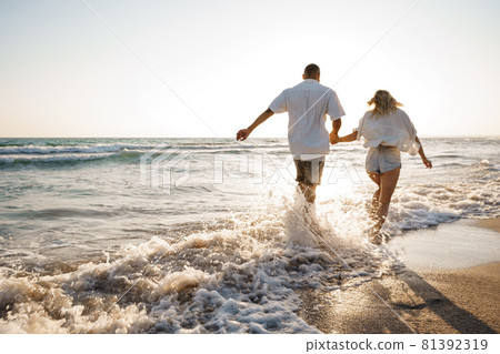 Young beautiful couple walking on beach near sea Young beautiful couple walking on beach near sea 81392319