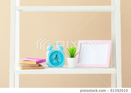 White bookshelf with books and stationery against beige wall White bookshelf with books and stationery against beige wall 81392610