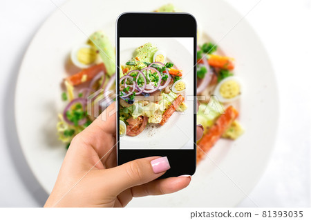 Photographing food concept - woman takes picture of fresh salad with lettuce, eggs, tomatoes, onion rings, peppers 81393035