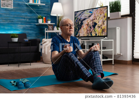 Senior man sitting comfortable in lotus position on yoga mat with closed eyes training body posture Senior man sitting comfortable in lotus position on yoga mat with closed eyes training body posture 81393436