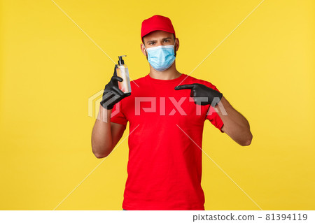 Covid-19, delivery orders, shopping, contactless handling and social distancing concept. Courier, takeaway employee in red uniform and medical mask, pointing at hand sanitizer Covid-19, delivery orders, shopping, contactless handling and social distancing concept. Courier, takeaway employee in red uniform and medical mask, pointing at hand sanitizer 81394119