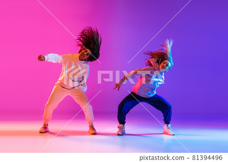 Two beautiful active girls dancing on gradient pink purple neon studio background Two beautiful active girls dancing on gradient pink purple neon studio background 81394496