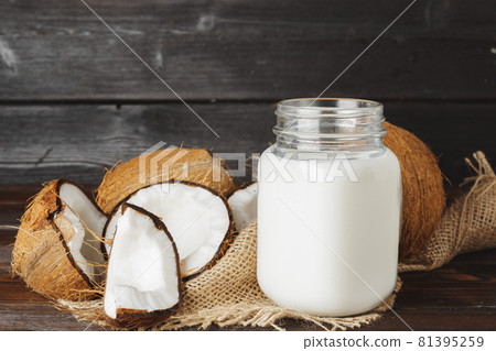 Broken coconut and coconut milk on black wooden background Broken coconut and coconut milk on black wooden background 81395259