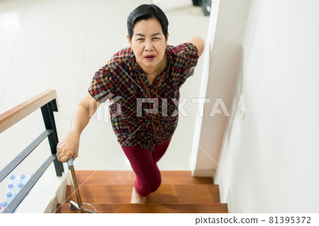 Asian senior older woman suffering from low-back lumbar pain while walking up on stair at home 81395372