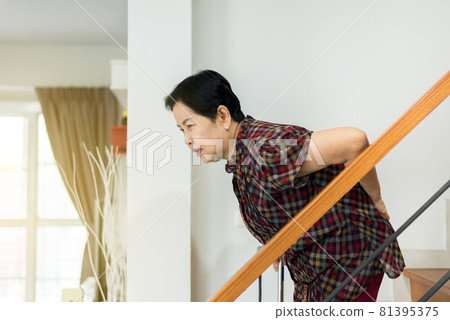 Asian senior older woman suffering from low-back lumbar pain while walking on stair at home 81395375