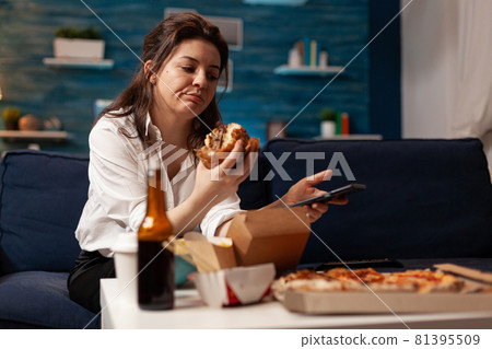 Caucasian female holding tastu burgery in hands browsing on social media using smartphone Caucasian female holding tastu burgery in hands browsing on social media using smartphone 81395509