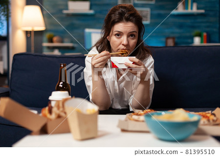 Portrait of caucasian female looking into camera while eating chinese chopstick relaxing on sofa Portrait of caucasian female looking into camera while eating chinese chopstick relaxing on sofa 81395510