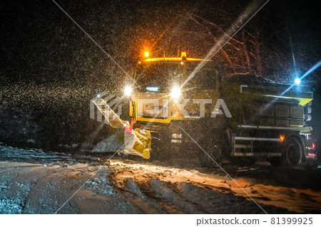 Highway maintenance truck cleaning road during heavy snowstorm in night, dangerous driving during winter transport calamity. 81399925